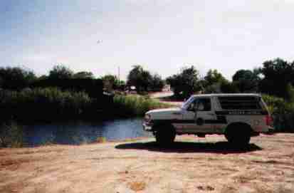 1993 Ford Bronco - A 1993 Ford Bronco, likely a Border Patrol vehicle, is parked by a body of water under a clear sky.