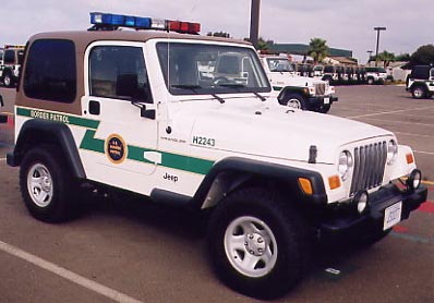 1993 Ford Bronco - A white Jeep Wrangler with a brown top and emergency lights is parked in a lot with other vehicles.