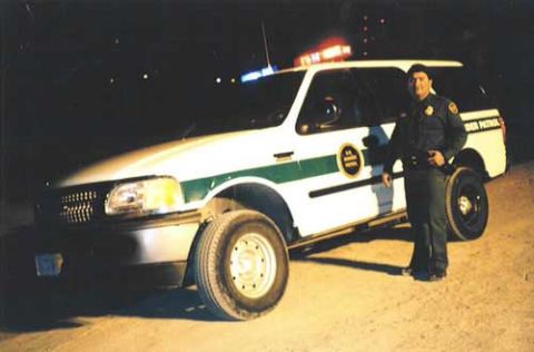 1993 Ford Bronco - A border patrol officer stands next to a white SUV with green stripes and "BORDER PATROL" markings, likely a 1995 model.