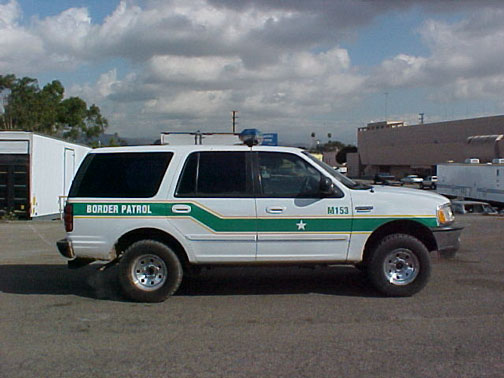 White Ford Expedition Border Patrol SUV in side profile with green stripe and unit number M153