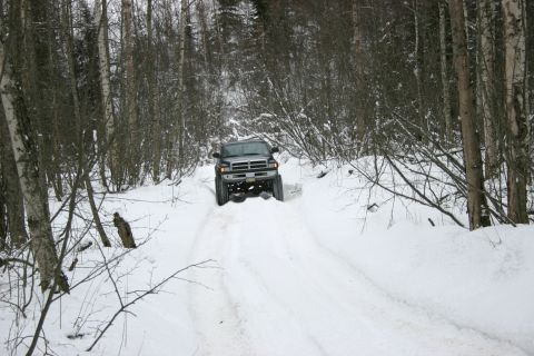 2003 Jeep TJ - A Dodge Ram pickup truck navigates a snow-covered path through a dense forest.