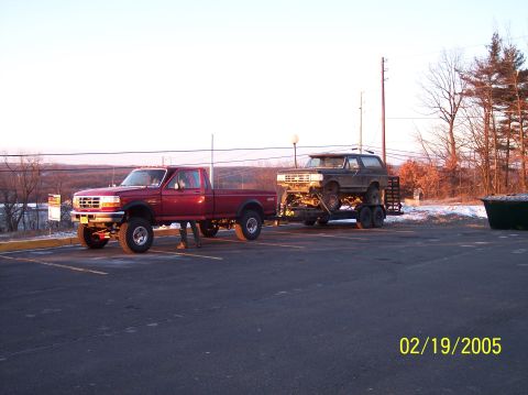 1995 Ford Bronco - A dark 1995 Ford Bronco is transported on a trailer towed by a red pickup truck.