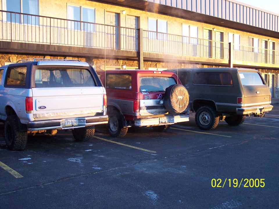 Three SUVs parked in a lot: a white Ford Bronco, a red Ford Bronco, and a dark green Chevrolet K5 Blazer. Date stamp reads 02/19/2005