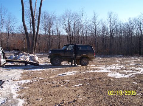 1995 Ford Bronco - A black Ford Bronco is parked in a dirt lot with trees in the background and snow on the ground.