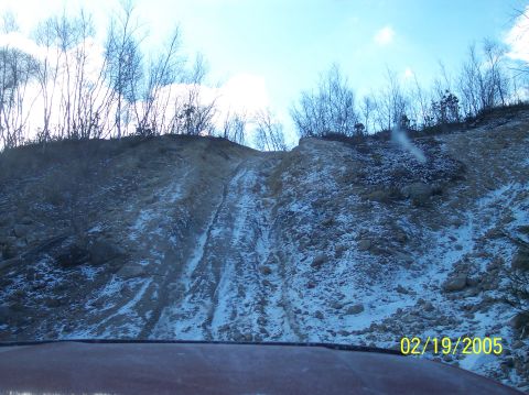 1995 Ford Bronco - A red Ford Bronco drives up a challenging, snowy, and muddy incline, leaving distinct tire tracks.