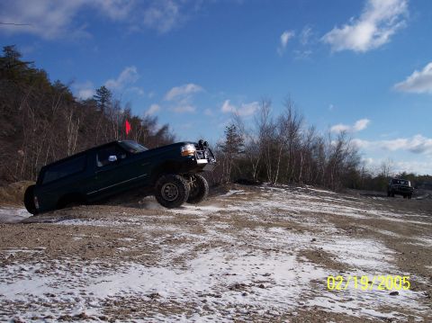 1995 Ford Bronco - A dark green 1995 Ford Bronco navigates a snowy, off-road terrain under a bright blue sky.