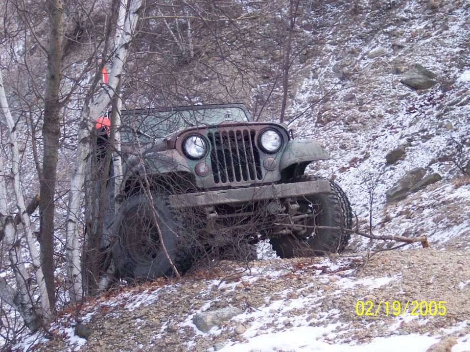 Camouflage Jeep stuck on a snowy, rocky incline
