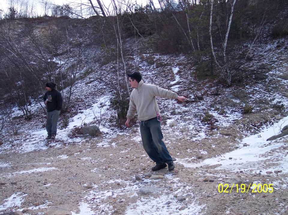 Two people stand in a rocky, snow-dusted landscape with bare trees