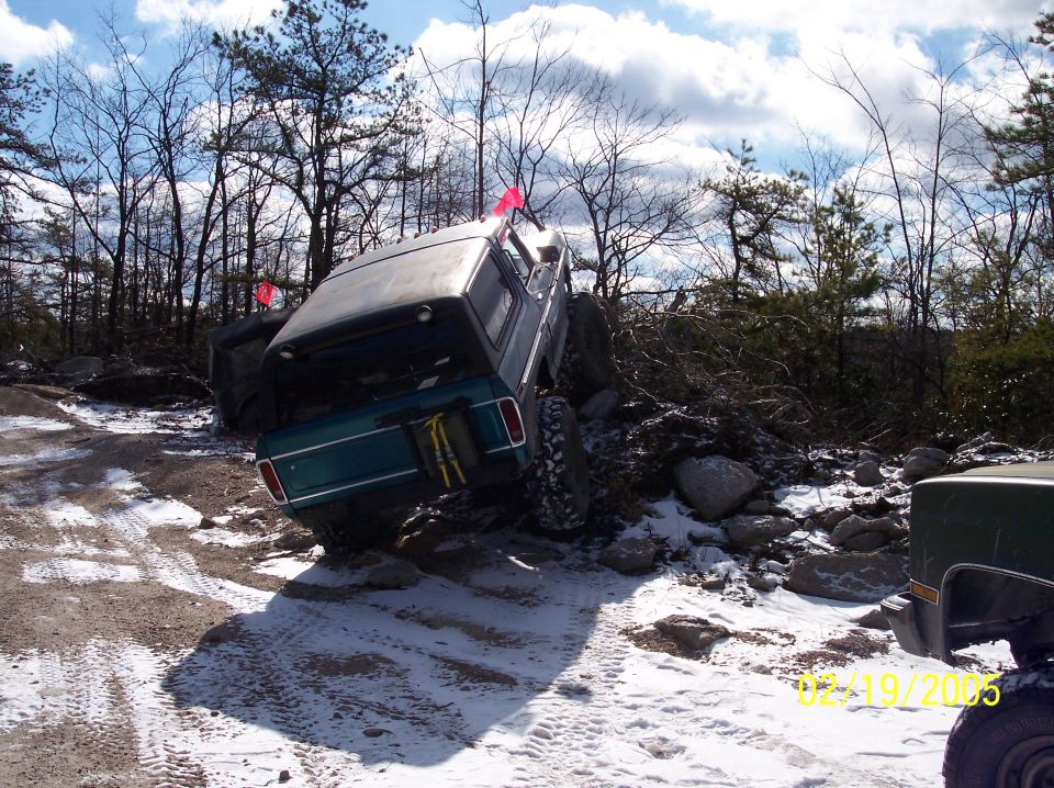 Green 1980 Ford Bronco off-roading on a snowy, rocky terrain