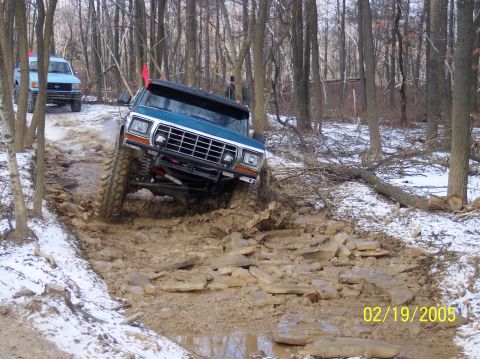 1995 Ford Bronco - A teal Ford Bronco tackles a challenging off-road course, with another blue vehicle visible in the background.