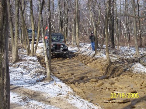 1995 Ford Bronco - Off-roading in a muddy forest trail with snow patches on the ground.