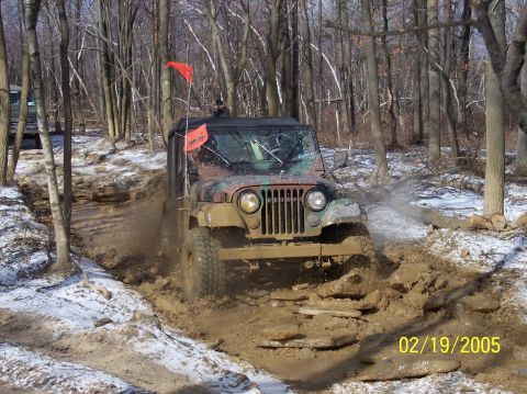 1995 Ford Bronco - Jeep CJ-7 navigates a muddy trail with snow on the ground.