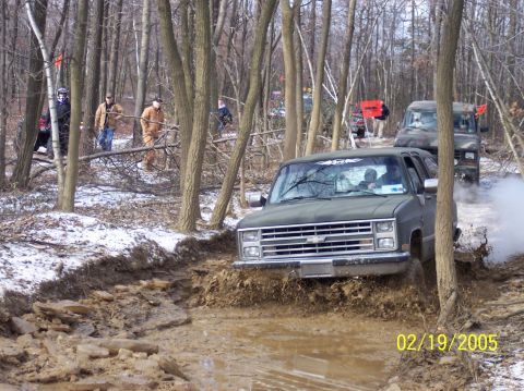 1995 Ford Bronco - Off-road vehicles navigate a muddy trail in a wooded area on a snowy day.