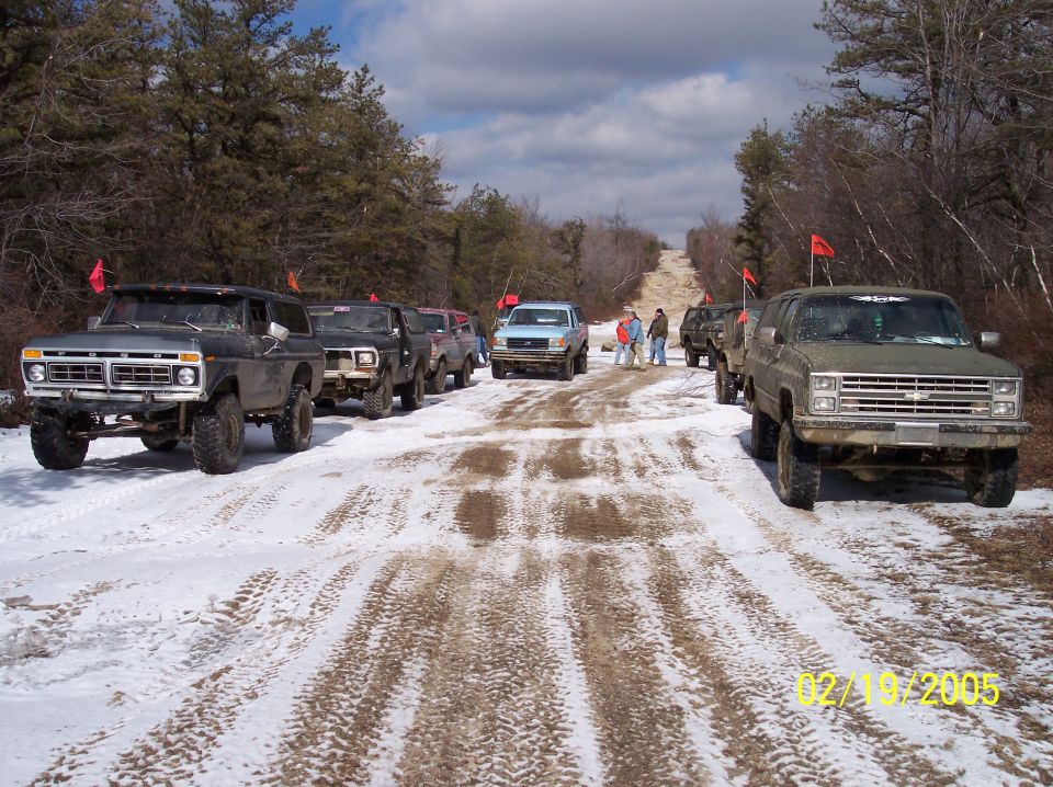 1977 Ford F-Series truck front view, lifted, with red flags on roof, in snowy landscape