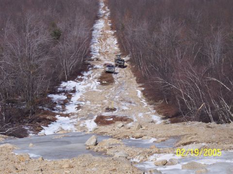 1995 Ford Bronco - Two SUVs traverse a difficult, muddy, and icy road through a wooded area on a winter day.