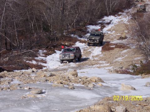 1995 Ford Bronco - A convoy of SUVs navigates a challenging icy and snowy trail in a wooded area.