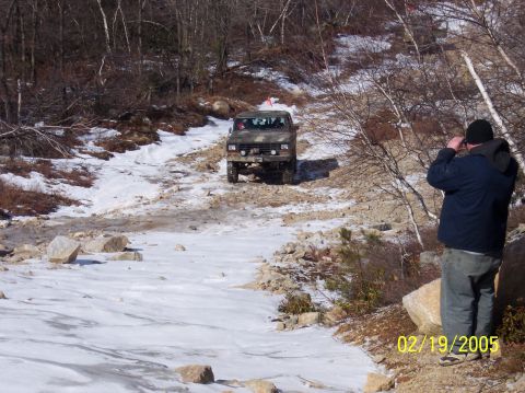 1995 Ford Bronco - A person observes an off-road vehicle navigating a challenging snowy and rocky terrain.
