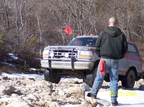 1995 Ford Bronco - A 1995 Ford Bronco navigates a challenging, rocky terrain, with a person observing the off-road adventure.