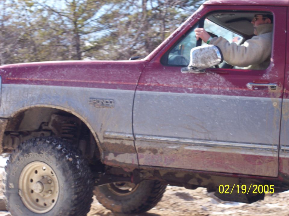 1995 Ford Bronco side view, driver visible, off-roading in dirt and trees