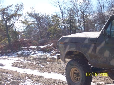 1995 Ford Bronco - A camouflaged Ford Bronco is seen on a rocky, snowy trail with trees in the background.