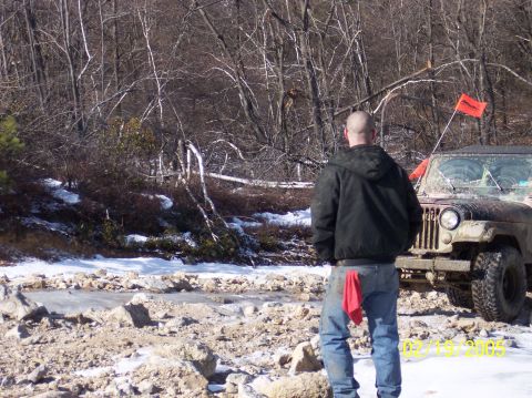 1995 Ford Bronco - Man watches a Jeep Wrangler navigate a snowy, off-road trail with an orange flag flying.