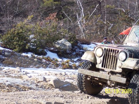 1995 Ford Bronco - A Jeep CJ navigates a snowy and rocky off-road trail on a sunny day.