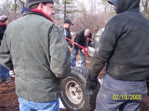 1995 Ford Bronco - A group of people work together to change a tire on a 1995 Ford Bronco in a wooded area.