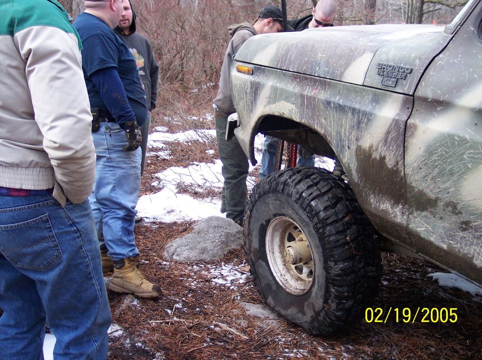 Camouflaged Ford Bronco, side view, with people standing around it in a wooded area. Date stamp 02/19/2005