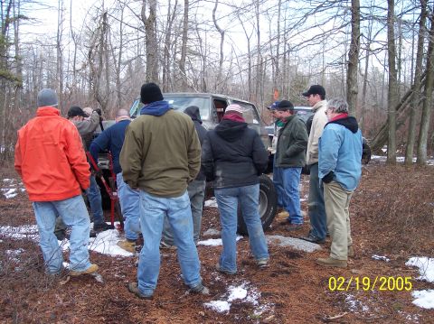 1995 Ford Bronco - A group of people stand around a vehicle in a wooded area, with snow visible on the ground.