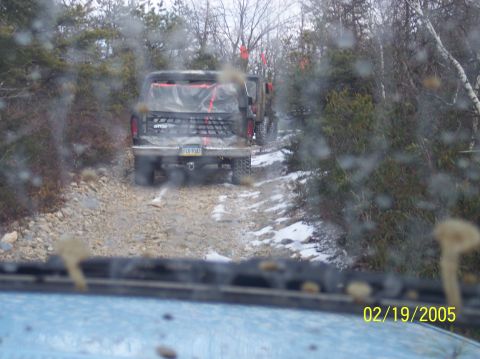 1995 Ford Bronco - Two SUVs navigate a snowy, rocky trail through a wooded area.