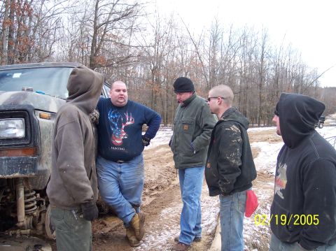 1995 Ford Bronco - A group of men stand around a muddy, camouflaged Ford Bronco in a wooded area during winter.
