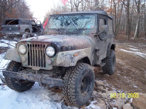 1995 Ford Bronco - A muddy camouflage Jeep CJ-7 sits in a snowy, wooded area with another SUV visible behind it.
