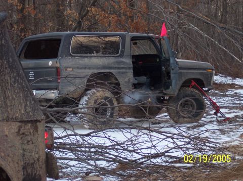 1995 Ford Bronco - This classic Ford Bronco is seen off-road with its door ajar, surrounded by wintery woods and fallen branches.