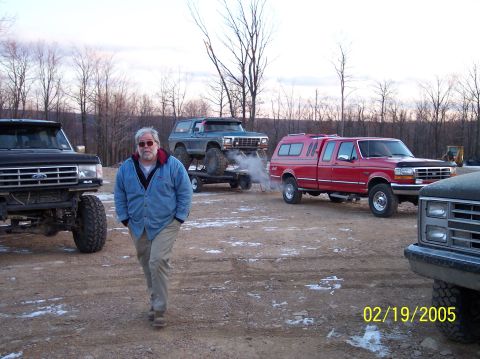 1995 Ford Bronco - Several trucks and a Bronco are parked outdoors on a dirt lot with a man walking in the foreground.
