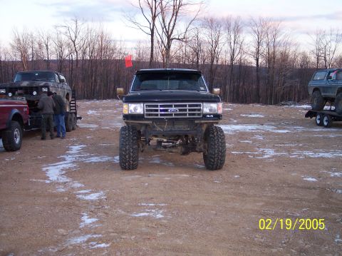 1995 Ford Bronco - Modified Ford truck with off-road tires parked outdoors with other vehicles on trailers.