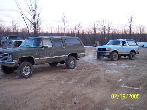 1995 Ford Bronco - A light blue 1987 Ford Bronco is parked on a dirt lot next to a dark green SUV.