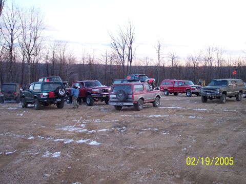 1995 Ford Bronco - A group of off-road vehicles are parked in a dirt lot on a cold day, with a red and silver 1995 Ford Bronco prominently featured.