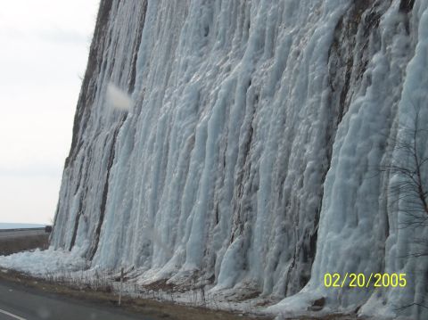 1995 Ford Bronco - A large cliff face is covered in ice formations, resembling a frozen waterfall, with a road visible at the bottom.
