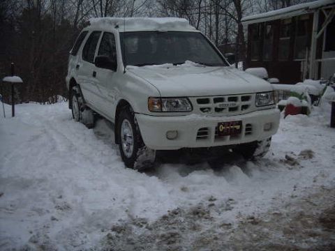 2000 Isuzu Rodeo - White 2000 Isuzu Rodeo covered in snow, parked outside a building.