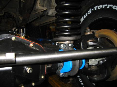 1992 Ford Bronco - Tight underside view of a lifted solid front axle showing a black coil spring seated on a spacer/shim at the axle perch, blue polyurethane…