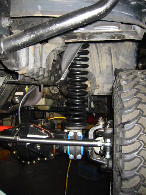 1992 Ford Bronco - Underbody close-up of a lifted truck's front suspension showing a black coil spring seated on the axle, the black-painted solid axle housin…