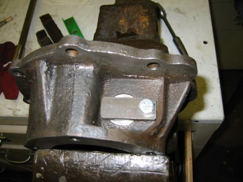 1992 Ford Bronco - A close-up view of a transfer case housing secured in a vise, showing a bolted metal plate on its side.
