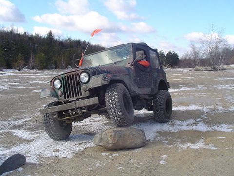 1995 Ford Bronco - Jeep CJ-7 navigating rough terrain with a rock under its front tire. Camo paint and off-road modifications are visible.