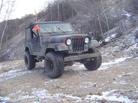 Camouflage Jeep CJ-5 on a dirt road with some snow