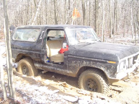 1995 Ford Bronco - A black Ford Bronco is stuck in a muddy wooded area, its driver's side door is open.