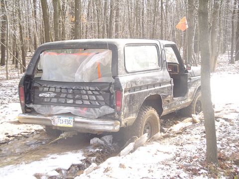 1995 Ford Bronco - This black Ford Bronco is stuck in a muddy, snowy wooded area, with its tailgate net visible.