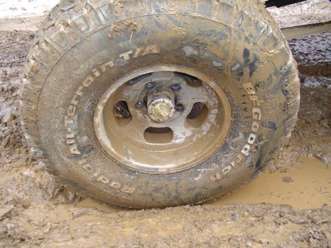 1995 Ford Bronco - A muddy BFGoodrich All-Terrain T/A tire and wheel is stuck in thick mud.
