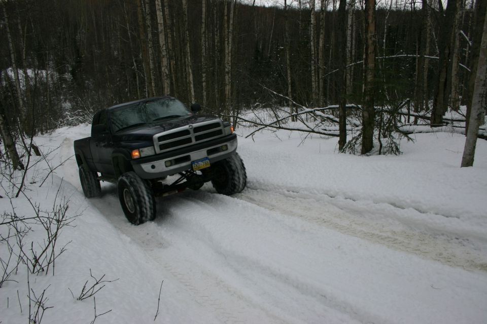 Dark blue pickup truck with lifted suspension driving on a snowy forest road