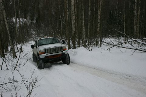 2003 Jeep TJ - White Ford F-250 Super Duty navigates a snowy path in a wooded area.