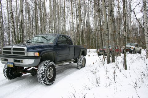 2003 Jeep TJ - Several trucks navigate a snow-covered trail surrounded by trees.